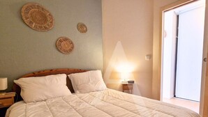 A neatly made bed with white bedding, a bedside lamp, and three woven wall decorations.
