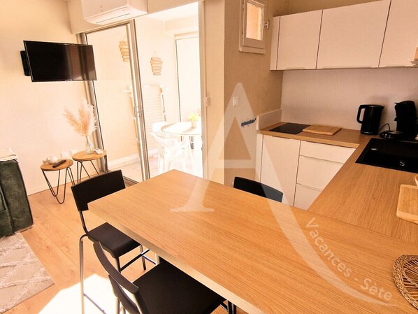 A modern kitchen with a wooden table and chairs, a built-in oven, and a coffee maker. - T2 CLASSÉ AVEC TERRASSE, VUE MER, CLIM (Sète)