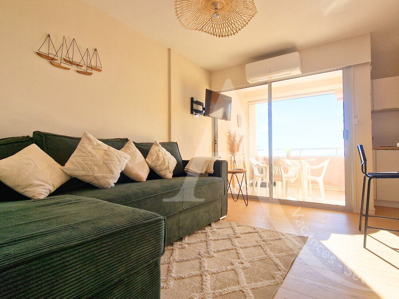A living room with a green sofa, a flat-screen TV, and a balcony with outdoor furniture.