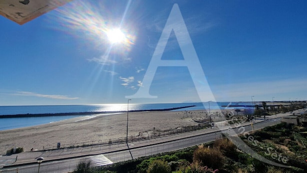 A beach with a clear sky, a road, and a large 'A' watermark.
