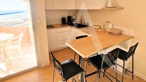 A modern kitchen with a wooden table and four chairs, a coffee maker, and a hanging light fixture.