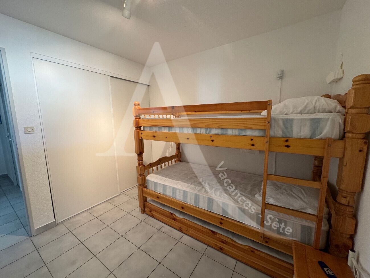 Un llit amb lliteres en una habitació de parets blanques i terra amb rajoles.