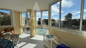 A sunlit balcony with a pool view, a dining table with chairs, and a small table with a bowl.