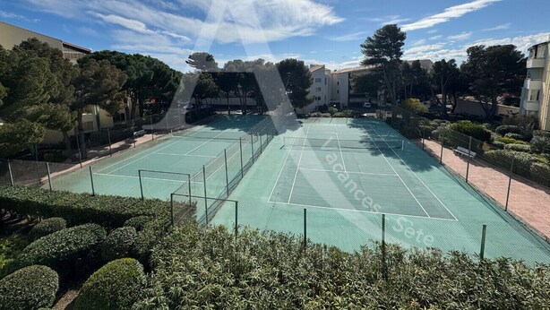 An outdoor tennis court surrounded by greenery and buildings.