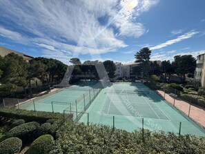An outdoor tennis court surrounded by greenery and buildings. - SPACIEUX APPT 2 CHAMBRES QUARTIER DES PLAGES (Sète)