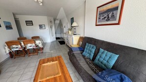 A living room with a sofa, wooden coffee table, dining table with chairs, and a lamp.