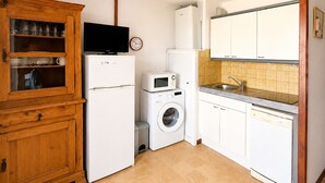 A compact kitchen with a wooden cabinet, a washing machine, a microwave, and a sink.