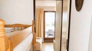 A room with a wooden bunk bed, a white sofa, a door leading to a balcony, and a tiled floor.