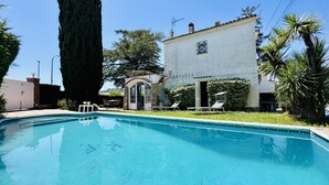 Ein Swimmingpool mit Liegestühlen, ein hoher Baum und ein Gebäude mit einem Schild.