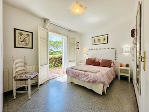 Un dormitorio con una cama, una silla, una mesita de noche y una puerta que da a un espacio exterior.