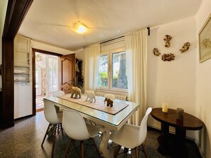 A dining area with a glass table, white chairs, and a small round table with a candle.