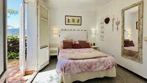 Ein Schlafzimmer mit einem Bett, Nachttischen, einem großen Spiegel, Wandkunst und Blick durch eine offene Tür.