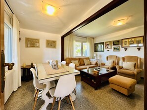 A living room with a dining table, chairs, sofas, a coffee table, and framed pictures on the walls.