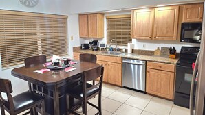 Una cocina con armarios de madera, lavavajillas de acero inoxidable, microondas y una mesa de comedor con sillas.