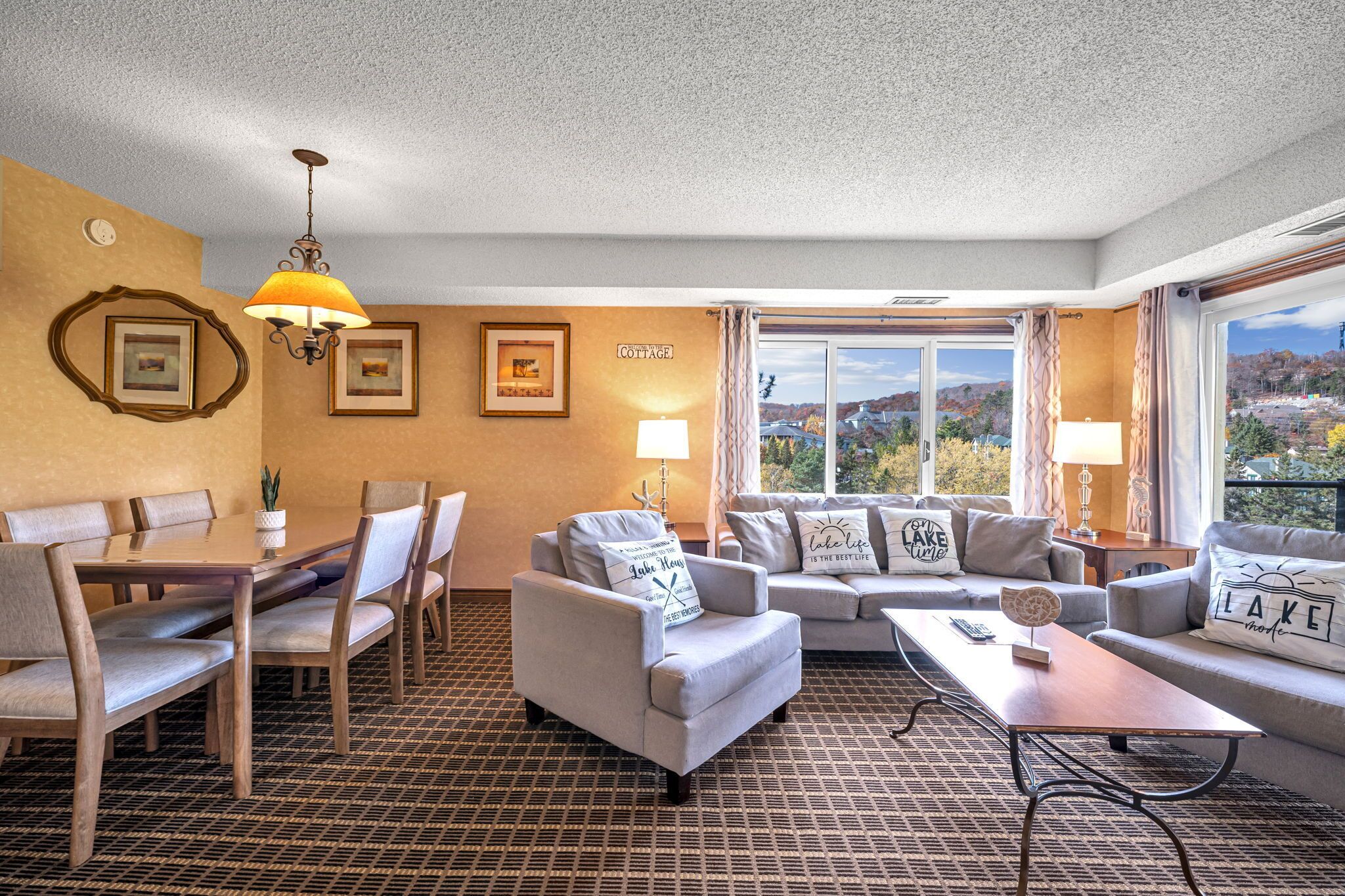 A hotel room with a dining area, a sofa set, a coffee table, and a view of the outdoors.