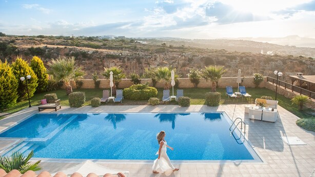 A swimming pool with a view of the landscape, outdoor seating, and a person walking by.