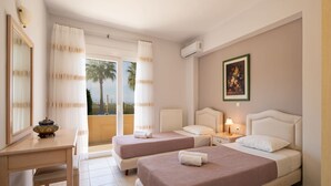 A hotel room with two beds, a desk, and a view of palm trees.