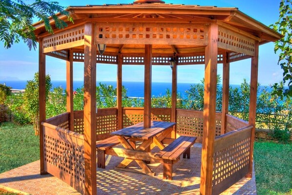 A wooden gazebo with a table and benches, surrounded by a garden and overlooking a scenic view. - KNOSSOS ESTATE, VILLA PASIFAI, a luxurious private villa with endless pool (Rethymno)
