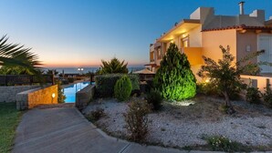 A modern villa with a swimming pool, surrounded by landscaped gardens and a clear view of the sunset.