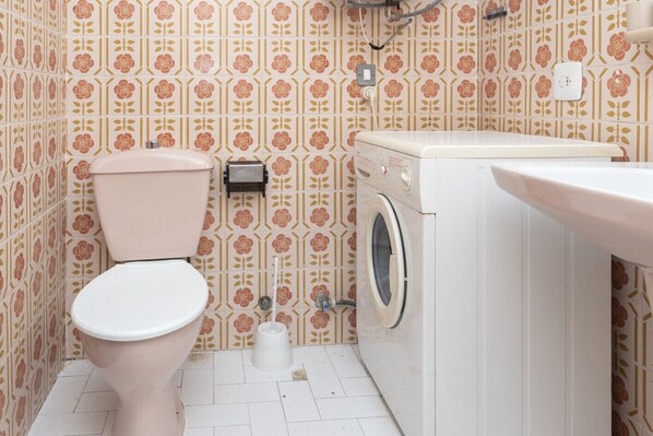 A bathroom with a toilet, washing machine, and sink.