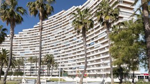 Een hotel met meerdere verdiepingen, een gebogen gevel, tal van balkons en palmbomen op de voorgrond.