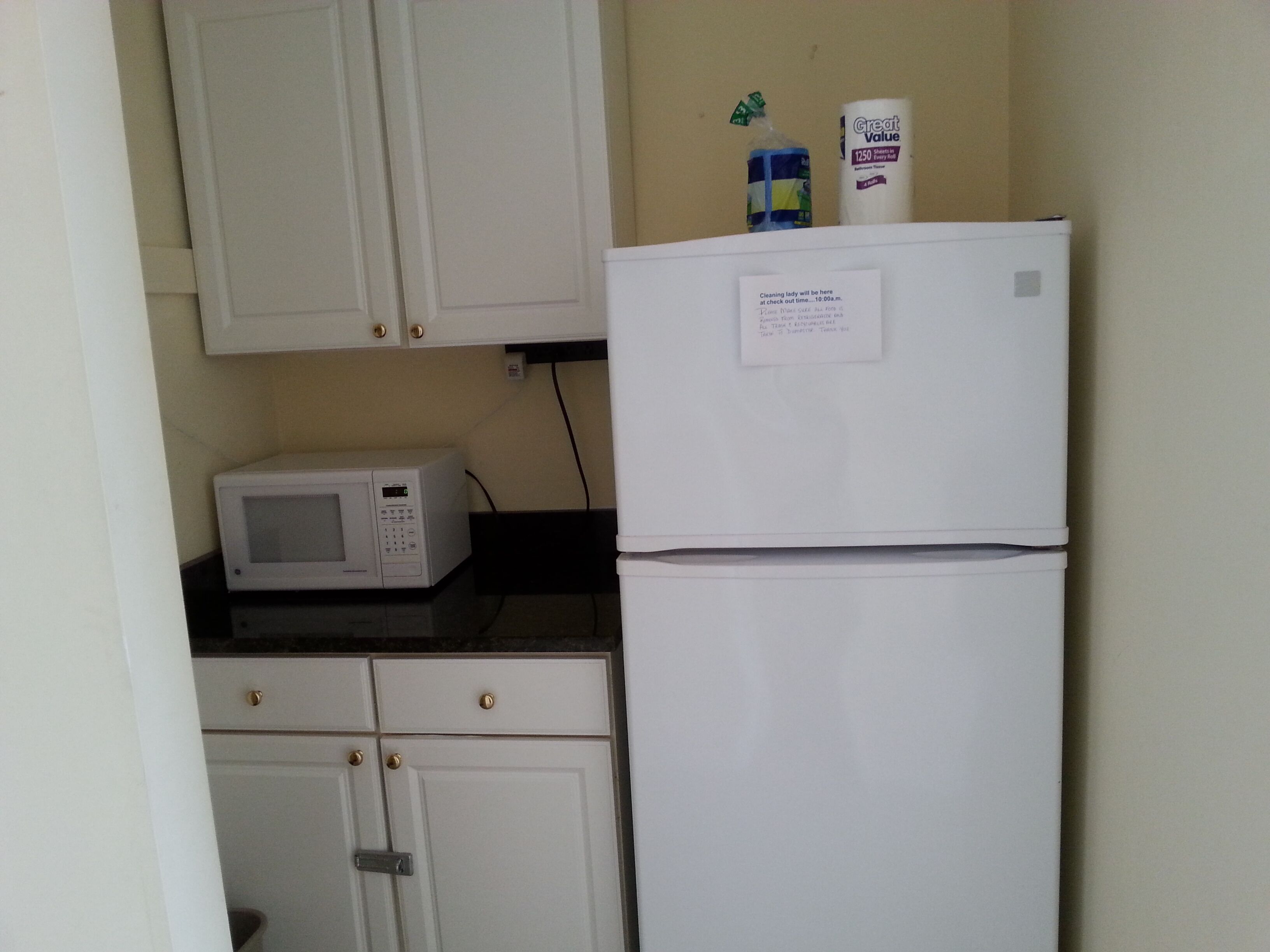 A compact kitchen with a white refrigerator, a microwave, and a cabinet with a lock.