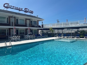 A hotel with a pool area, outdoor seating, and a sign reading "Carriage Stop". - Beachfront Condo (Wildwood Crest)