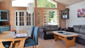 Interior acogedor de una cabaña con una mesa de comedor, dos sofás, una mesa de centro de madera y un armario con puertas de cristal.