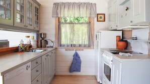 Una cocina compacta con gabinetes de madera, una ventana con cortinas, una cafetera y una estufa.