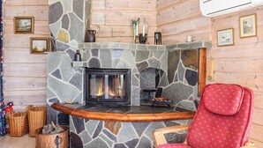 Interior acogedor de una cabaña con chimenea de piedra, paredes de madera y un sillón tapizado en rojo.