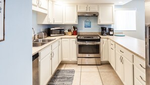 A modern kitchen with white cabinets, stainless steel appliances, a toaster, a coffee maker, and a hanging sign. - Highly rated Condo in Ocean Front Community, Wheelchair accessible, Dog friendly (St Augustine Beach)