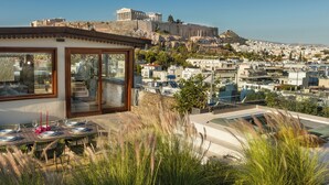 Un edificio moderno con terraza y vistas a un paisaje urbano y ruinas antiguas.