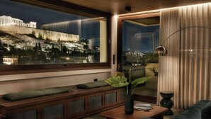 Una sala moderna con un ventanal grande con vistas a un paisaje urbano, un banco empotrado con cojines, una mesa de centro y una lámpara de pie.