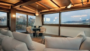 Una sala de estar moderna con ventanas amplias, un sofá y una mesa con sillas.
