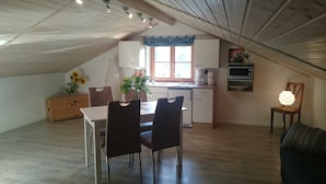 Ein Essbereich mit Tisch und Stühlen, eine Küche mit Fenster und eine Decke mit freiliegenden Balken.