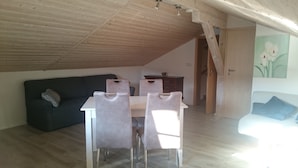 Ein Zimmer mit Holzbalkendecke, einem dunklen Sofa, einem Esstisch mit Stühlen und einem Bild an der Wand.