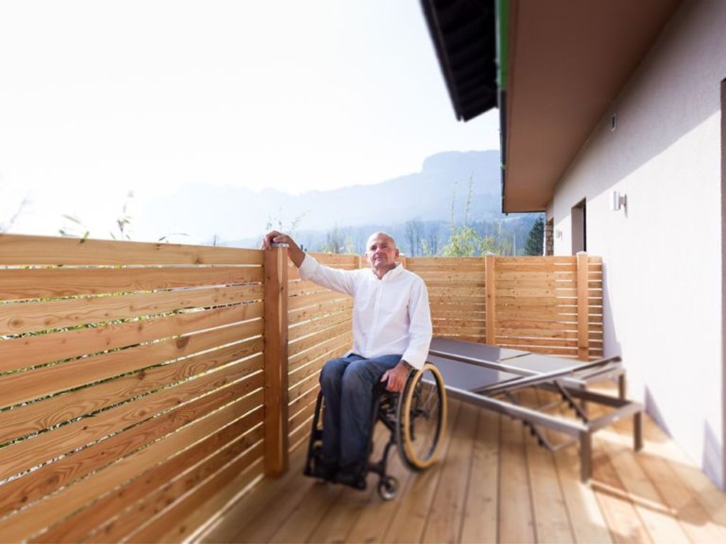A person in a wheelchair on a wooden deck with a view of mountains.