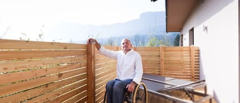 A person in a wheelchair on a wooden deck with a view of mountains.