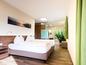A modern hotel room with a large bed, a bedside table, a wall-mounted artwork, and a potted plant.