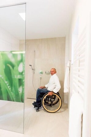 Une salle de bain accessible aux personnes en fauteuil roulant, dotée d’une paroi en verre, d’une douche et d’un porte-serviettes.
