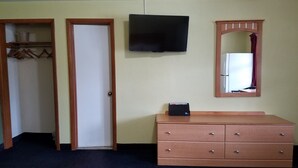 Une pièce avec une commode en bois, un téléviseur fixé au mur et un miroir au-dessus.