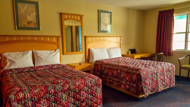 Une chambre d’hôtel avec deux lits, un bureau, une chaise et une fenêtre avec des rideaux.