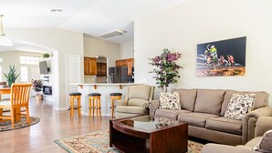 Uma sala de estar ampla com um sofá grande, uma mesa de centro e uma área de jantar com cadeiras e mesa de madeira.