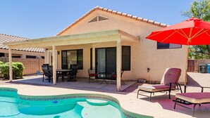 Um alpendre coberto com piscina, móveis de exterior e um guarda-sol vermelho.