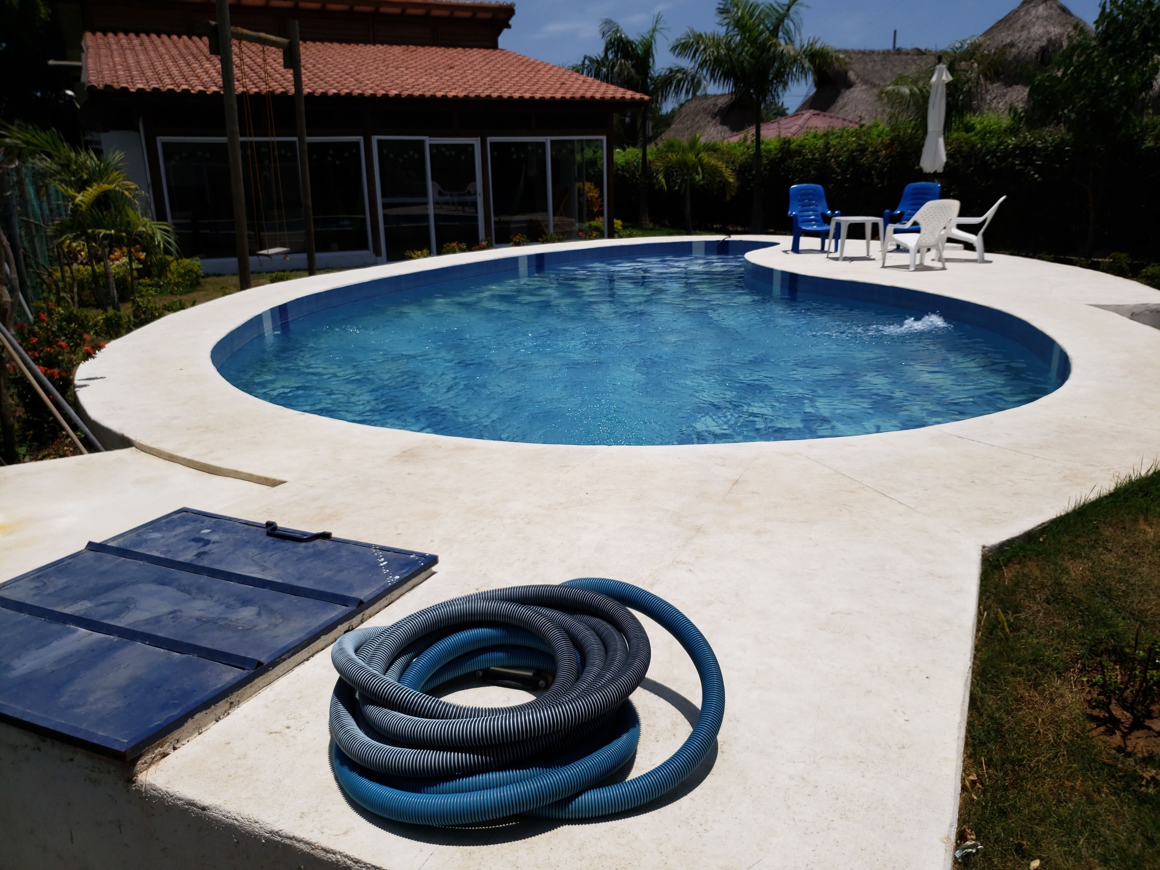 Una piscina de borde curvo, rodeada por un solárium de hormigón. Hay sillones de descanso y una mesa con sombrillas.