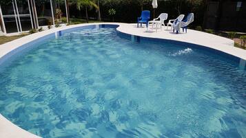 A swimming pool with clear blue water, surrounded by lounge chairs and a covered seating area.