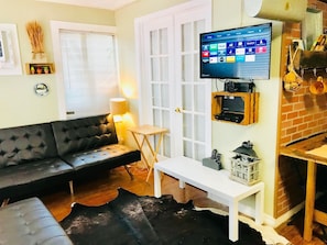A living room with a black leather sofa, a white coffee table, a TV mounted on the wall, and a small wooden shelf with electronic devices. - Nice Apartment/East Hollywood/2 miles to beach/Sleep 6/Free Parking/BBQ/J-7 (Hollywood)
