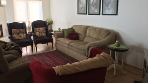 Un salón con un sofá color crema, un sillón rojo y un sofá marrón. Hay tres cuadros en la pared, una mesita con una manzana verde y una alfombra roja en el suelo.