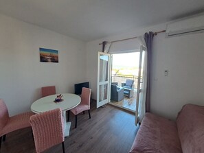 Una stanza con un tavolo rotondo, sedie rosa, un divano, una TV e un balcone con mobili da esterno.