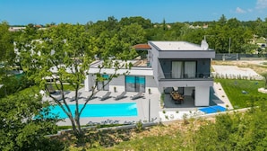 Ein modernes, zweistöckiges Haus mit Swimmingpool, Außenbereich zum Sitzen und Blick ins umliegende Grün.